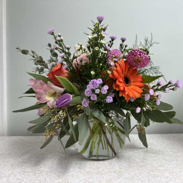 Mixed bouquet in a clear glass vase with orange, pink, and purple flowers
