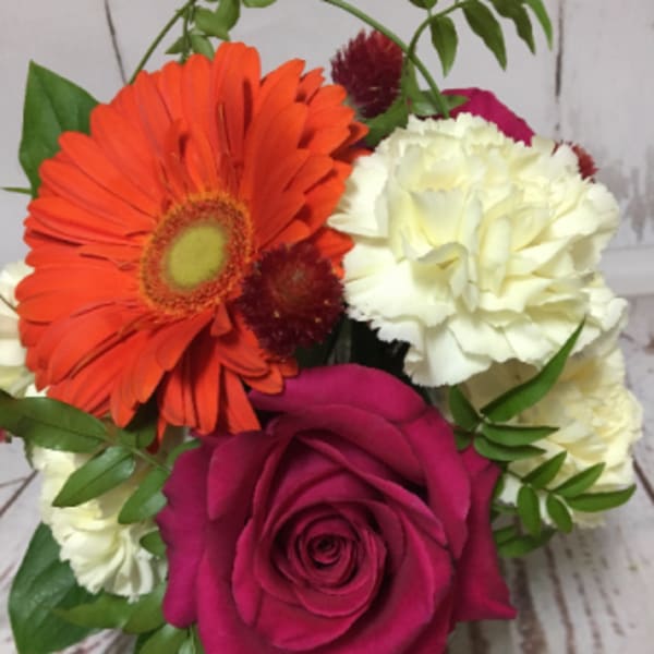 Compact arrangement with orange gerbera, pink rose, white carnations, and red accent blooms.