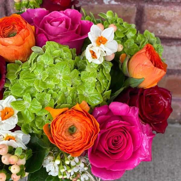 Bouquet of pink, red, and orange roses with green hydrangeas and small white flowers