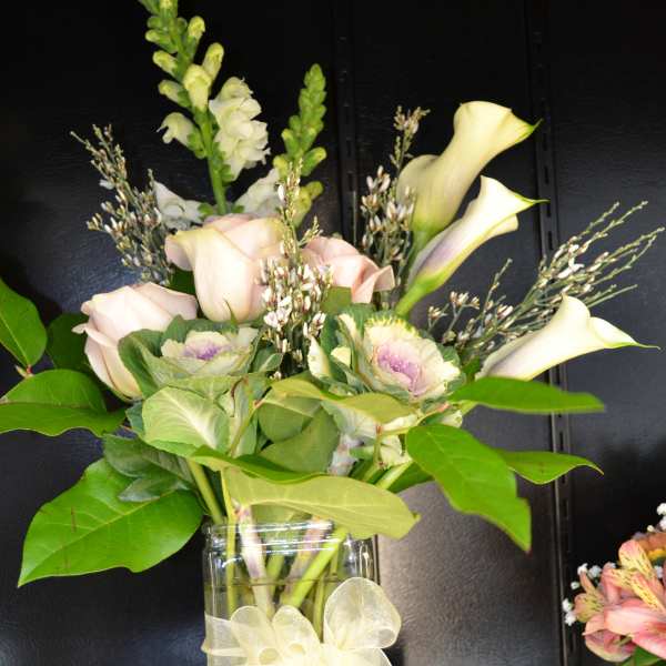 Bouquet of pale roses and calla lilies in a glass vase with a ribbon bow