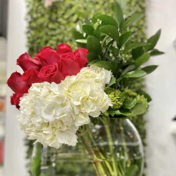 Asymmetrical arrangement of red roses and white hydrangeas in a round clear glass bowl vase