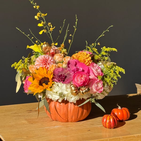Mixed flower arrangement in a pumpkin-shaped container with small decorative pumpkins