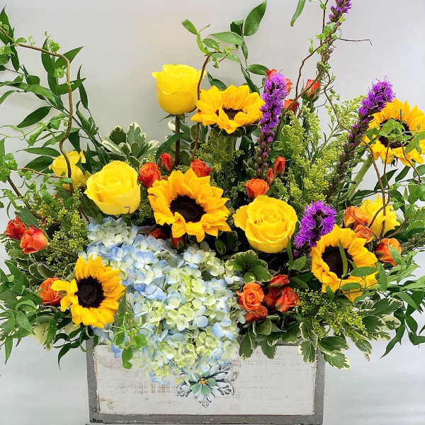 Bright mixed bouquet with sunflowers, yellow roses, and blue hydrangeas in a white box
