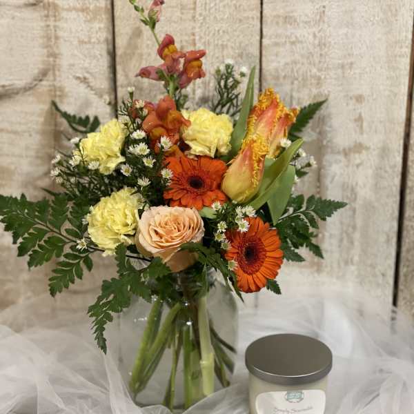 Mixed bouquet in a glass vase beside a scented candle