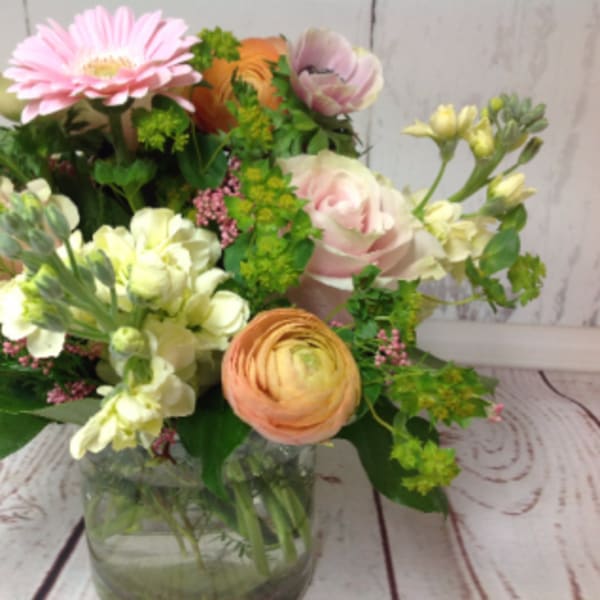 Mixed arrangement of pink, peach, and cream flowers in a clear glass vase on a wood surface
