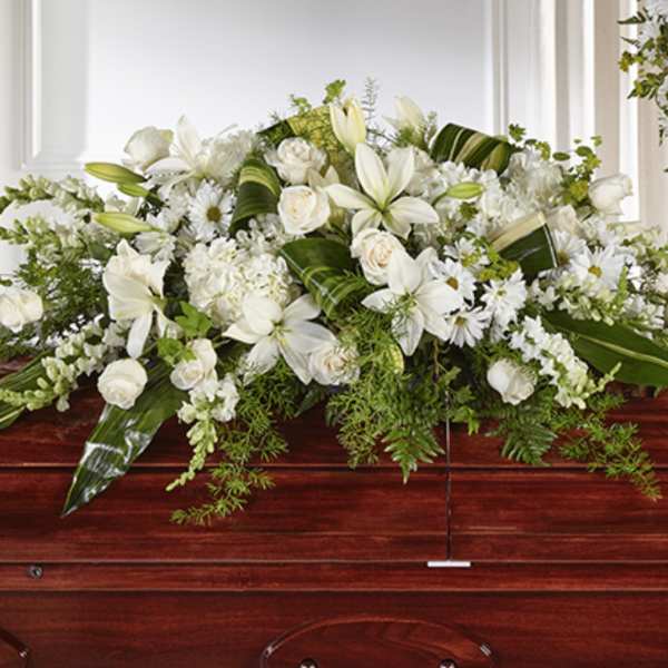 White lily and rose casket spray with mixed white flowers on a dark wood casket