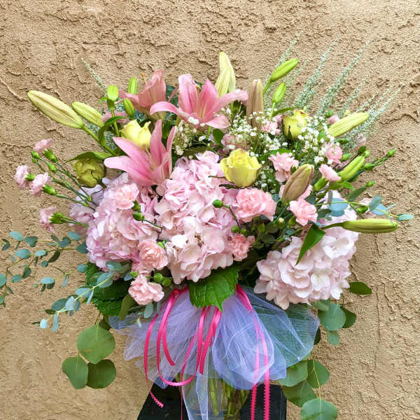Pink and yellow mixed bouquet with lilies, roses, and hydrangeas in a glass vase