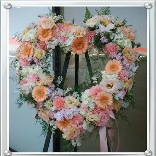 Heart-shaped floral wreath with pink, peach, and white flowers on an easel