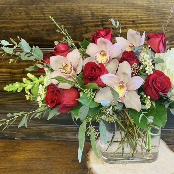 Bouquet of red roses, pale orchids, and white hydrangea in a glass vase