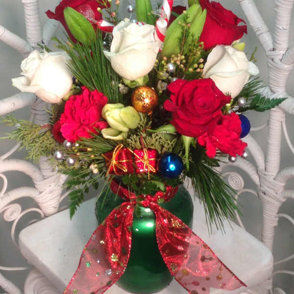 Red and white roses in a green vase with holiday ornaments and ribbon
