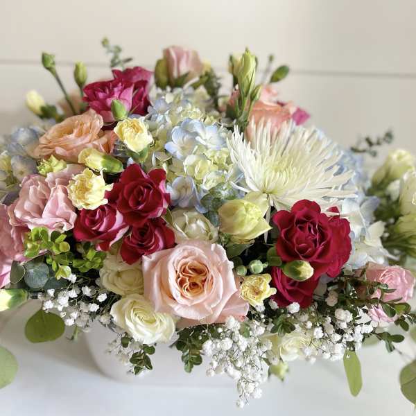 Mixed bouquet of pink, red, and white flowers in a low white container
