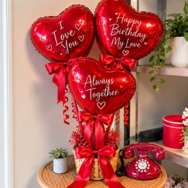 Three red heart-shaped balloons with birthday and love messages in a basket