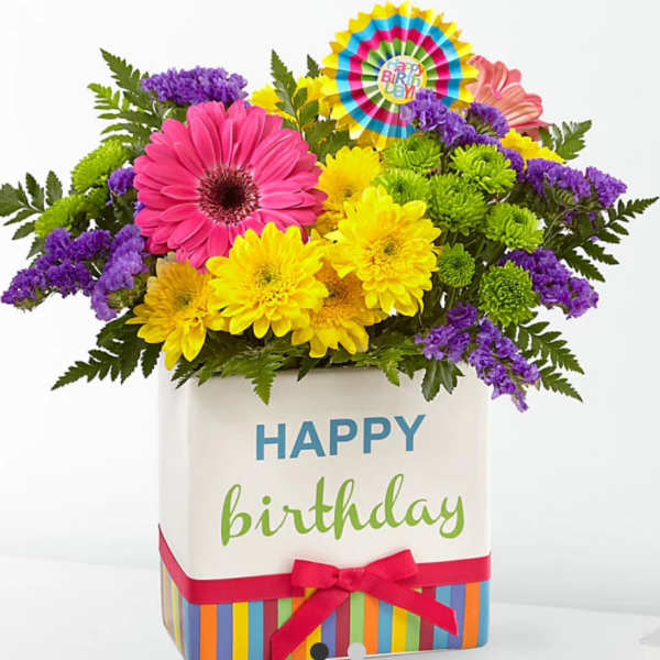 Bright birthday bouquet with pink gerbera, yellow blooms, and purple accents in a happy birthday cube vase