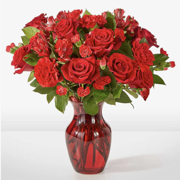 Red roses and carnations arranged in a red glass vase