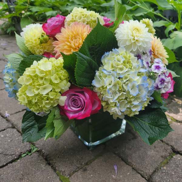 Mixed bouquet of hydrangeas, roses, and dahlias in a glass vase