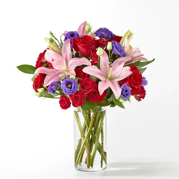 Bouquet of red roses, pink lilies, and purple blooms in a clear glass vase