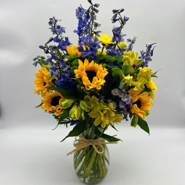 Bouquet of sunflowers, blue delphinium, and yellow alstroemeria in a glass vase
