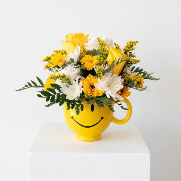 Yellow and white flower arrangement in a smiley-face mug