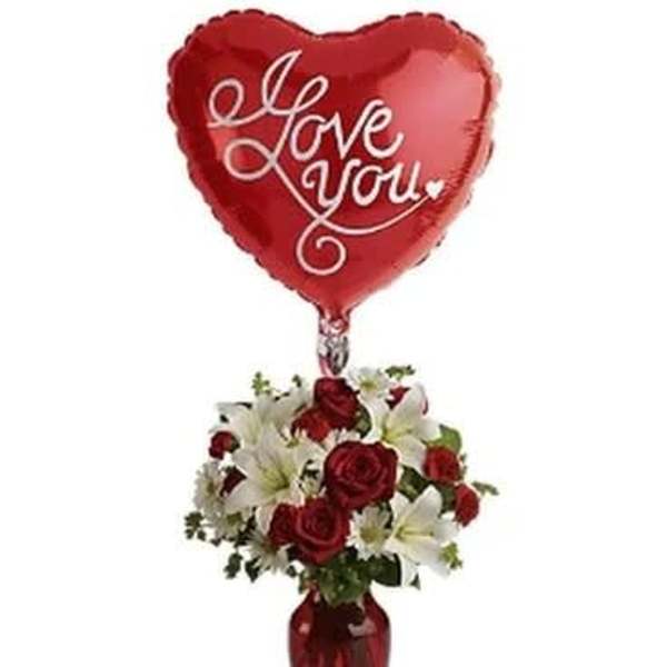 Heart-shaped red balloon above a vase of red roses and white lilies