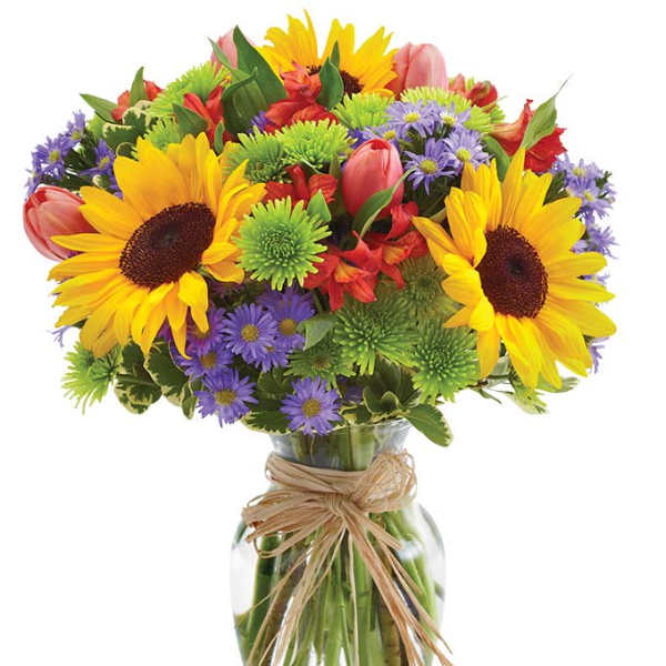 Bright mixed bouquet of sunflowers, tulips, and purple daisies in a glass vase