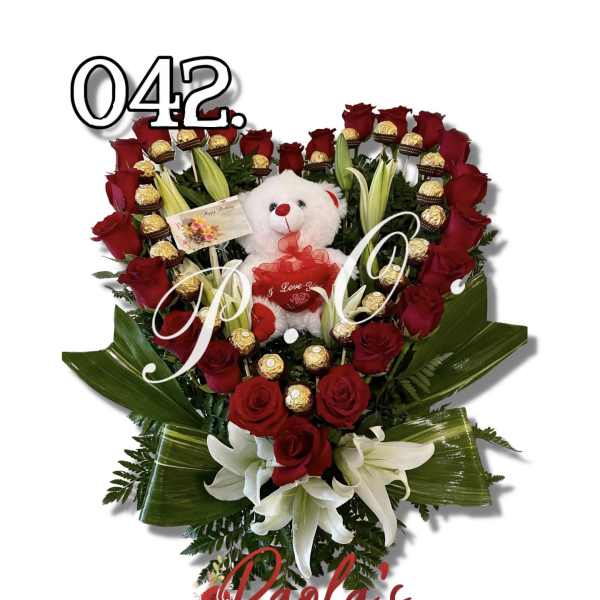 Heart-shaped bouquet of red roses with lilies, chocolates, and a teddy bear