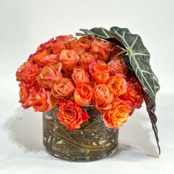 Orange rose bouquet in a clear glass vase with dark leaves