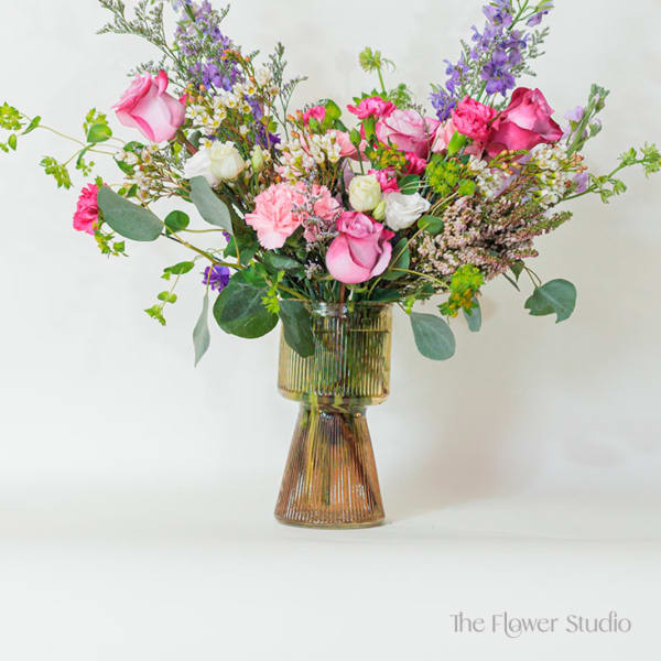 Tall mixed arrangement of pink roses, carnations, and purple flowers in a ribbed glass vase