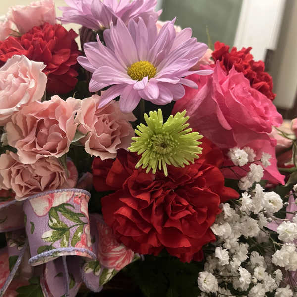 Mixed bouquet of pink, red, and lavender flowers with a patterned ribbon