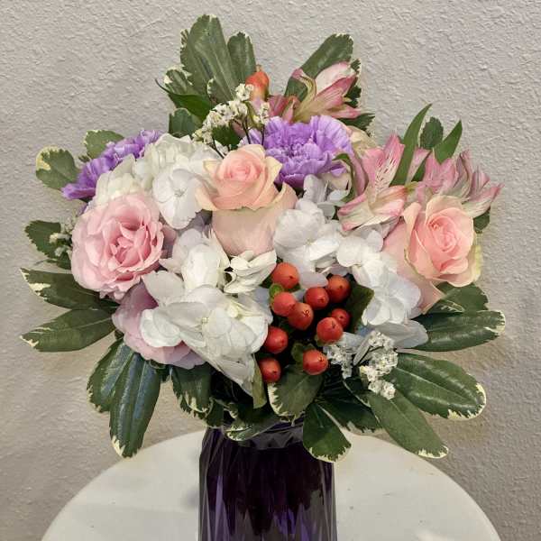Pink and white mixed bouquet with purple accents and red berries in a faceted dark purple glass vase