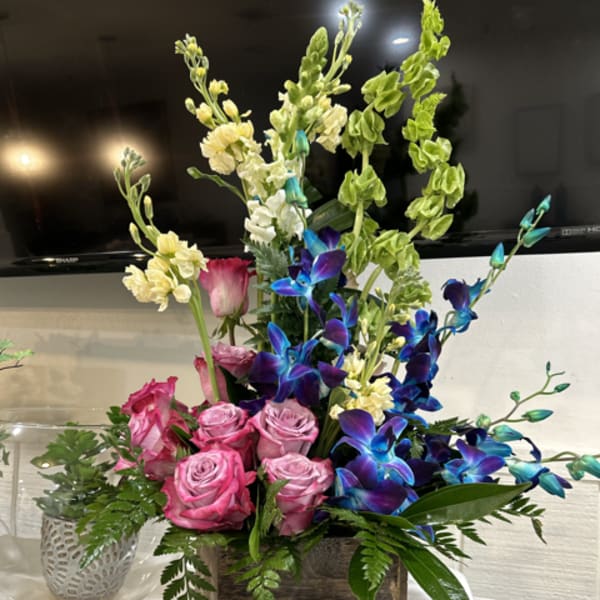 Pink roses and blue orchids in a wooden box with greenery