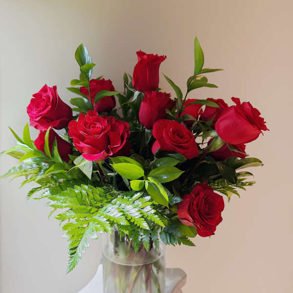 Red roses arranged in a clear glass vase with fern foliage