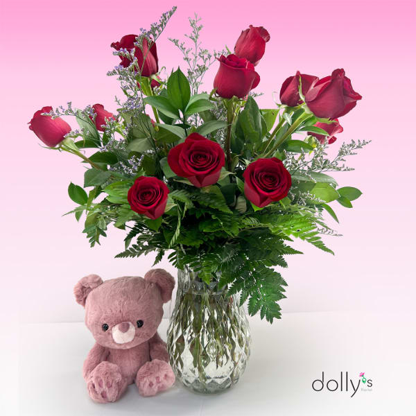 Red roses in a glass vase with a pink teddy bear beside it