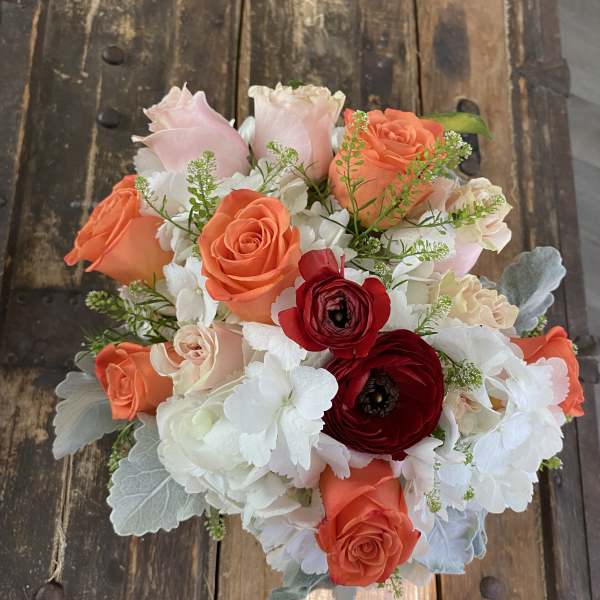 Bouquet of coral and blush roses with white blooms on a rustic wood surface