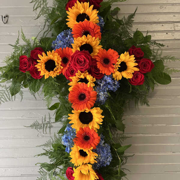 Cross-shaped floral arrangement with sunflowers, gerbera daisies, roses, and blue hydrangeas