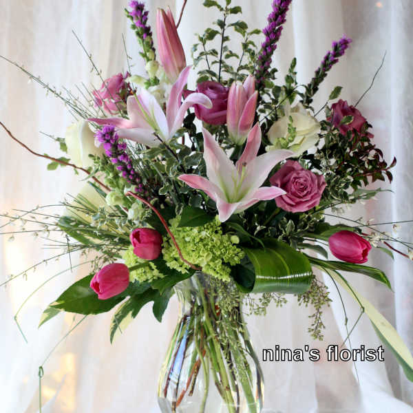 Pink lilies and roses arranged in a clear glass vase