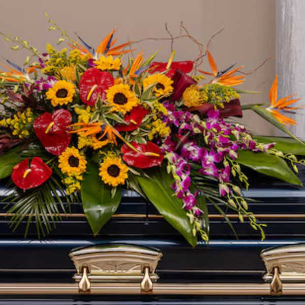 Tropical casket spray with yellow sunflowers, red blooms, purple orchids, and orange birds of paradise.