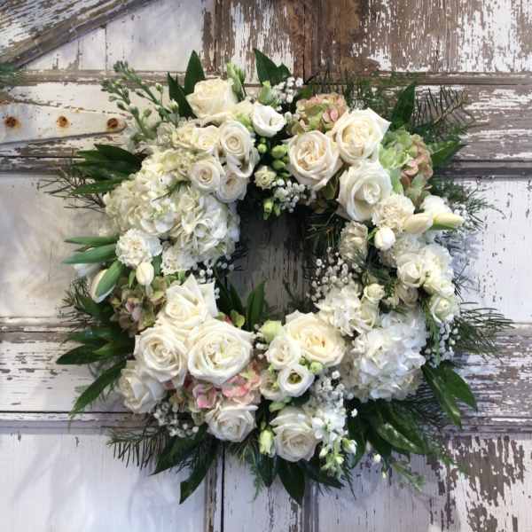 White floral wreath with roses and hydrangeas on a rustic door