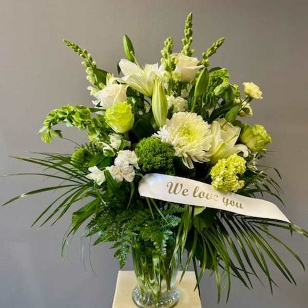 White and green sympathy arrangement in a glass vase with a "We love you" ribbon