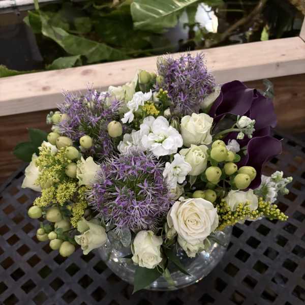 Bouquet of white roses, purple allium, and dark calla lilies in a glass vase