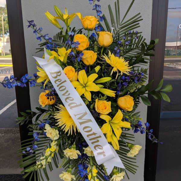 Yellow and blue floral standing spray with a "Beloved Mother" ribbon