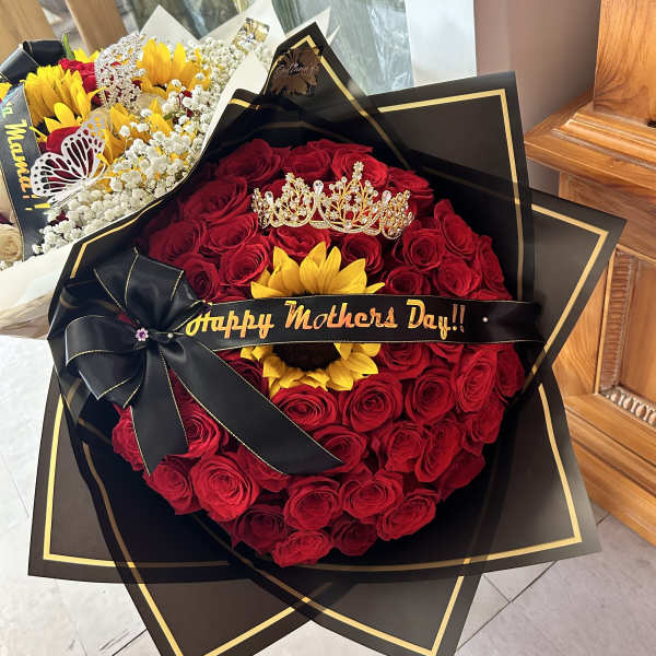 Red rose bouquet with a sunflower, crown, and black ribbon reading Happy Mother's Day