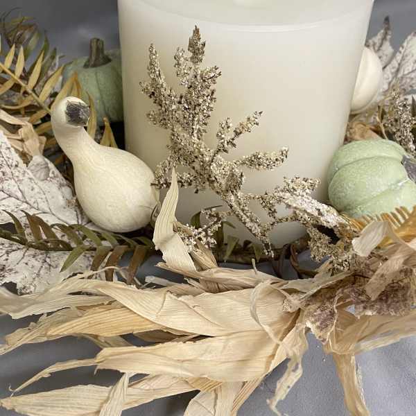 Large white pillar candle surrounded by dried foliage and decorative gourds