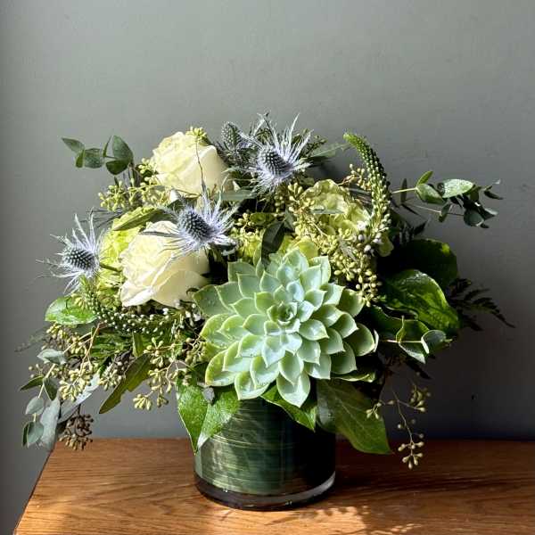 Succulent arrangement with white roses and blue thistles in a green vase