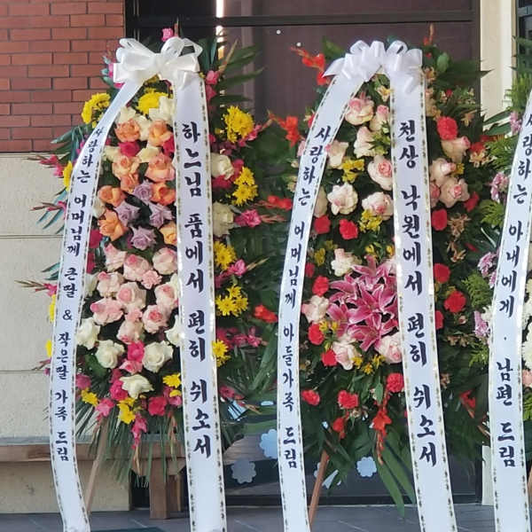 Three tall floral standing wreaths with white ribbon banners and mixed blooms