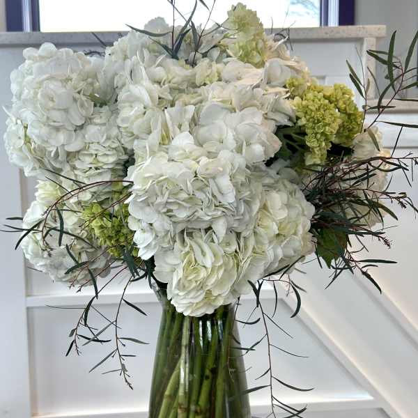 White hydrangea arrangement in a glass vase with pebbles