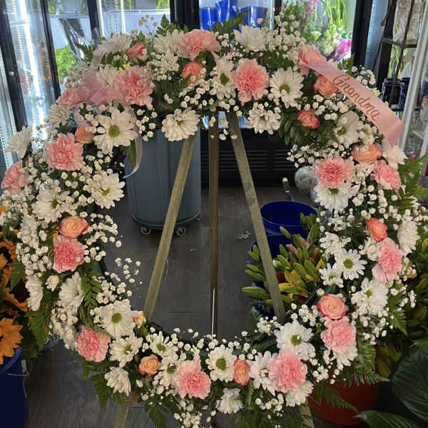 Large pink and white floral wreath on a stand with a ribbon