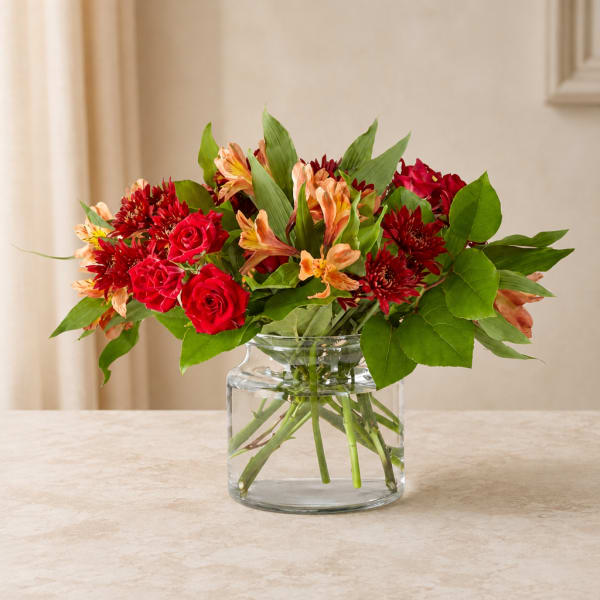 Red roses and orange flowers arranged in a clear glass vase