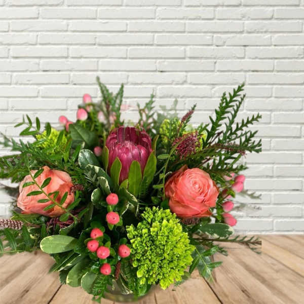Mixed bouquet with pink blooms and a magenta protea in a low vase
