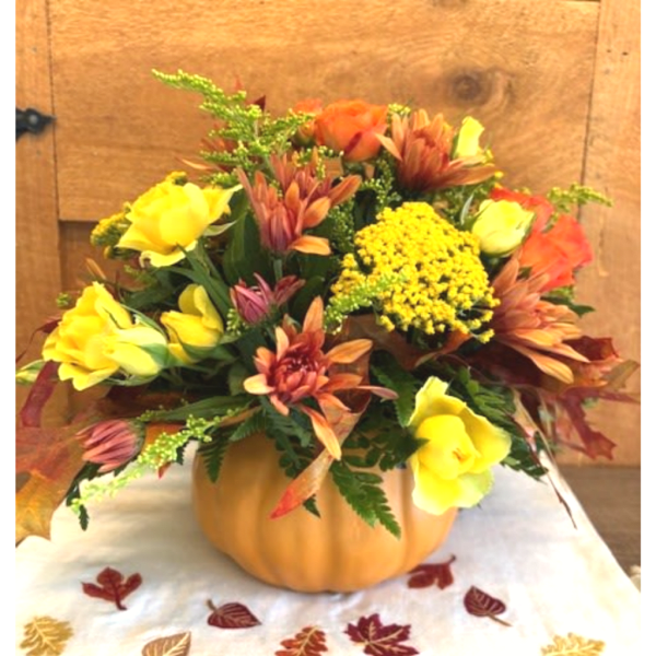 Autumn flower arrangement in a pumpkin-shaped container with yellow and orange blooms