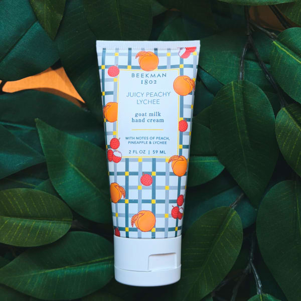 Tube of Beekman 1802 Juicy Peachy Lychee hand cream on dark green leaves